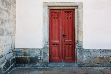 Red wooden door on stone building exterior with ornate carvings