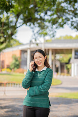 Asian female student in warm clothes using phone to chat with friends and ready for video call while in university.