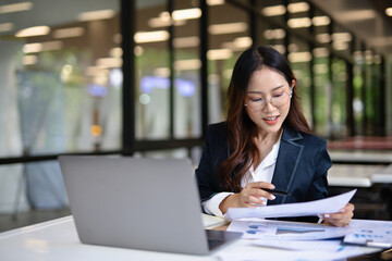 Asian businesswoman working on financial market research using laptop and digital tablet about digital investment in office.