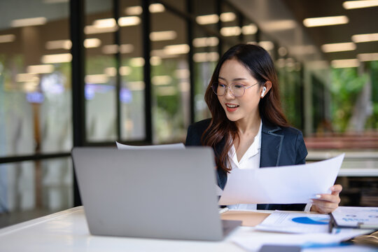 Asian businesswoman doing financial market research using laptop and digital tablet on digital investment in front of modern office.