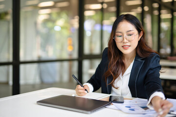 Obraz premium Asian businesswoman working on financial market research using laptop and digital tablet about digital investment in office.