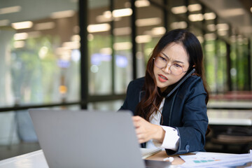 Asian businesswoman working on financial market research using laptop and digital tablet, stressed...