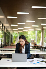 Fototapeta premium Asian businesswoman working on financial market research using laptop and digital tablet, stressed about digital investment in office.