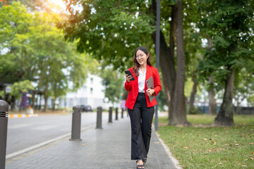 Asian businesswoman in suit using mobile phone while standing in front of modern business building.