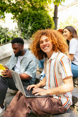 College student using laptop on campus steps with friends