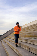 Young brunette woman in her early 20s, fit and sporty, wearing leggings and a top, using her phone with headphones on, selecting music to get motivated before her workout.