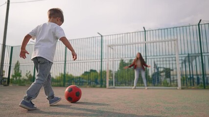 Family playing soccer with ball park. Child kicks red soccer ball while family holds hands. Fun family activity outdoors. Parents and child enjoy bonding time. Soccer game in park with family and ball