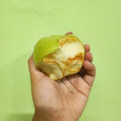 A bitten green  held in a hand against a light green backdrop.