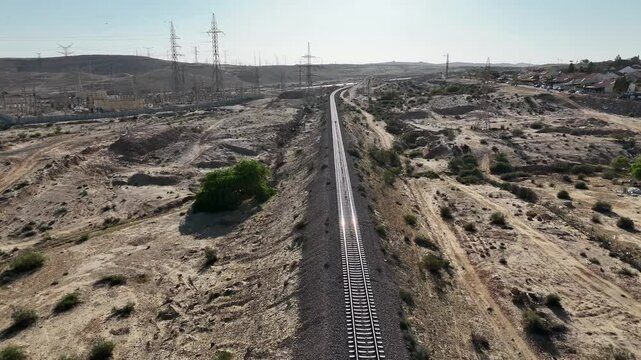 Aerial view of a remote desert railway cutting through sandy terrain, with parallel tracks