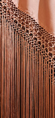 Close-up of intricate macramé detailing with long, flowing fringe in a warm copper hue, attached...