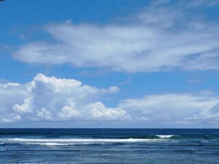 A calm blue sea with gentle white waves under a bright blue cloudy sky.
