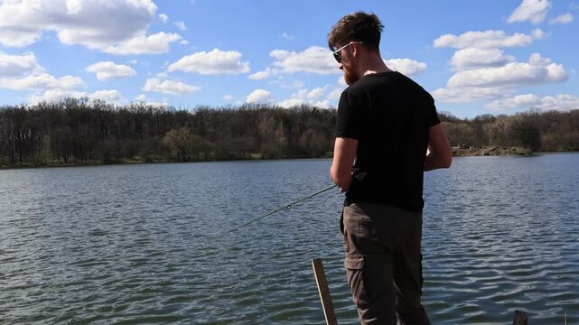 Fisherman on wooden pier casting spinning rod on sunny river