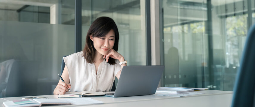 Young businesswoman professional employee using pc doing online banking analysing at workplace. Asian middle-aged business woman working on laptop computer in office, taking notes. Banner, copy space