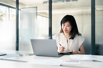 Middle-aged Asian woman using laptop computer for business studying, watch online virtual webinar training meeting, video call. Focused mature saleswoman businesswoman working in office, copy space.