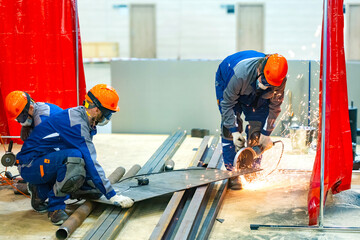 Team of workers in safety gear cutting metal sheet with angle grinder, producing sparks in an...