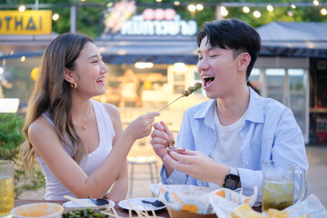 Smiling woman feeding her partner with street food during their travel dining experience.