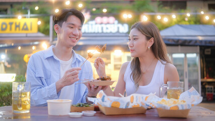 Young travelers tasting local grilled skewers and snacks at a vibrant outdoor food stall.