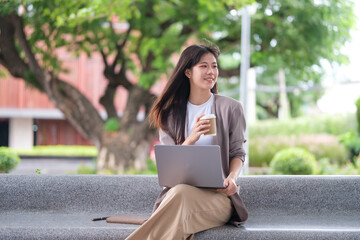 Young businesswoman enjoying coffee while working on her laptop outdoors in a peaceful urban setting.