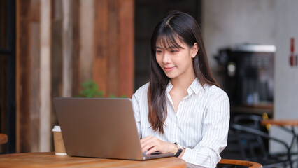 Confident young businesswoman working on a laptop at a cozy coffee shop.