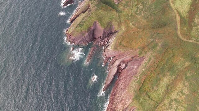 Waves washing jagger rocky coast. High angle view, tilt up reveal panoramic view of sea shore. South Wales, UK