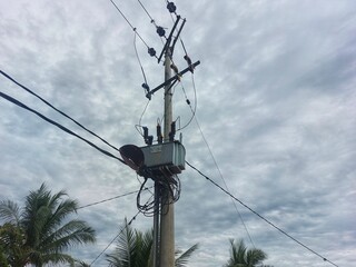 An electric utility pole with a transformer and power lines against a cloudy sky
