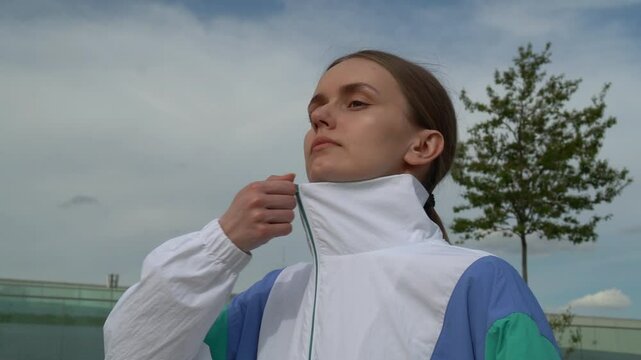Close-up of a fit young woman zipping up her zip-up jacket outdoors after workout. Showing focus and cool-down moment in sportswear.