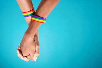 Gay couple with rainbow striped wristbands holding hands when standing against blue background with...