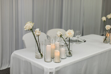 Bridal wedding table decorated with white roses and ivory candles for bride and groom with white backdrop