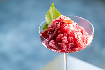 A refreshing strawberry granita served in a glass, garnished with fresh strawberries and a mint...