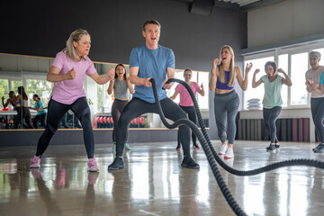 A focused man trains with battle ropes as his friends support him during an intense workout session in the gym Sports and motivation concept