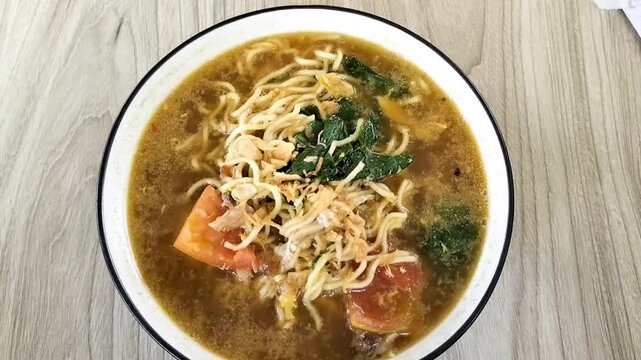 A bowl of boiled noodles complete with vegetables, chicken pieces and eggs on a wooden table. Spicy javanese noodles with soup that are perfect for eating on rainy nights.