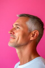 Fototapeta premium Pink solid background. A smiling man in a professional portrait session. Visual idea of style for aging men. Elegant men's mid fade haircut - midlife white man with hair.