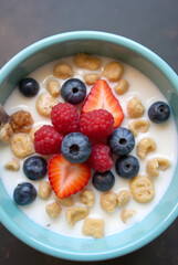 Close-up of breakfast cereal with berries, strawberries, blueberries and milk in a blue bowl
