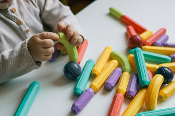 Toddler playing with colorful magnetic building sticks and balls on a white table, developing fine motor skills and creativity through sensory learning