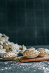 Close-up of uncooked dumplings sprinkled with flour, arranged on a dark countertop with a wooden board, capturing a rustic homemade cooking moment