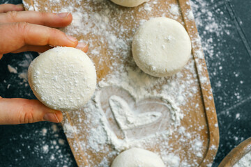 Close-up of a hand holding a raw dough round over a floured kitchen counter with baking tools in the background