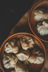 Two clay bowls filled with traditional dumplings placed on a rustic burlap cloth over a dark...