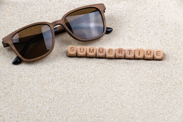 Sunglasses on sandy beach with wooden blocks spelling summertime