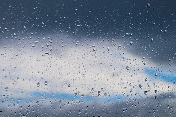 Rain drops on window with cloudy sky in background