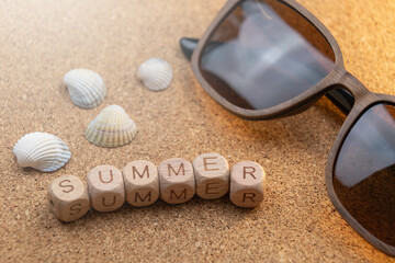 sunglasses and seashells on cork background. Wooden blocks spelling summer