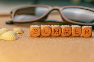 Sunglasses and seashells on cork background with wooden blocks spelling summer