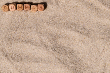Wooden letter blocks spell 'summer' on sandy beach background