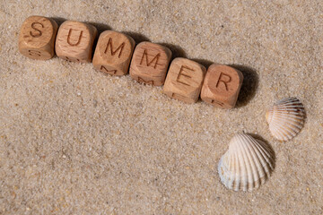 Beach sand with Wooden letter blocks spell 'summer' and seashells