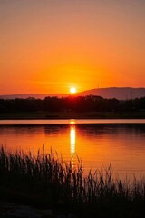 Naklejka premium sunset over a lake with a boat in the water and a mountain in the distance