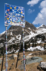 The Staller saddle, Austria - May 2 2025: Border sign at Staller Pass (Austria-Italy) covered in colorful stickers, set against snow-dusted alpine peaks under a bright blue sky.