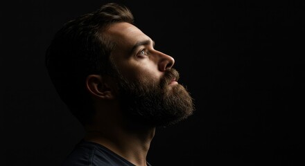 Profile Portrait of a Bearded Man Looking Upward - A contemplative man, beard shadowed, gazes skyward, symbolizing hope, introspection, faith, resilience, and dreams. Dark background enhances mood