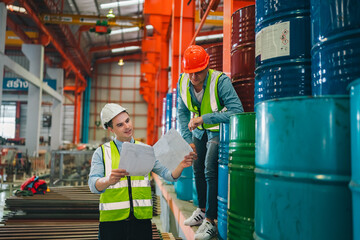 Industrial engineers inspect liquid storage drums in large-scale warehouse for export logistics,...