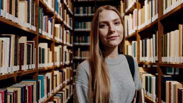 Young woman exploring cozy library aisle and selecting books for study session
