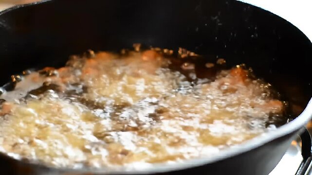 Chicken pieces deep frying in hot oil in a cast iron skillet