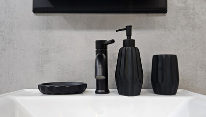 Black faucet, ceramic bottles for soap or shampoo and glass for toothbrushes or mouthwash on white shelf for sale. Object on gray wall background with copy space.